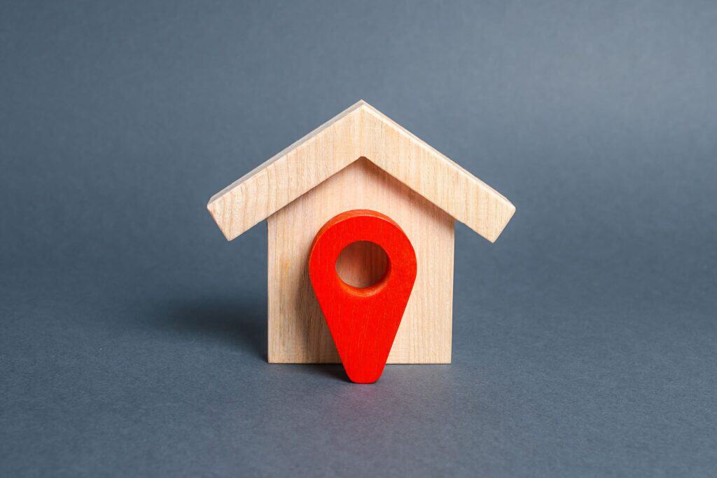 A wooden house figurine with red location pointer