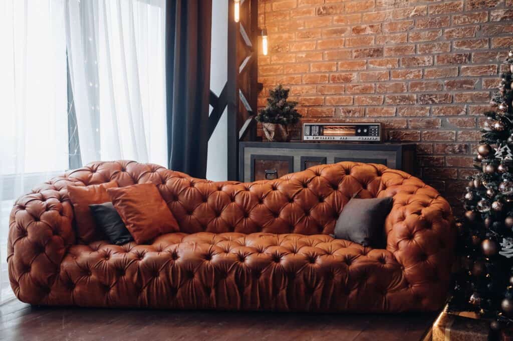 A large awkwardly shaped couch in a living room with brick walls